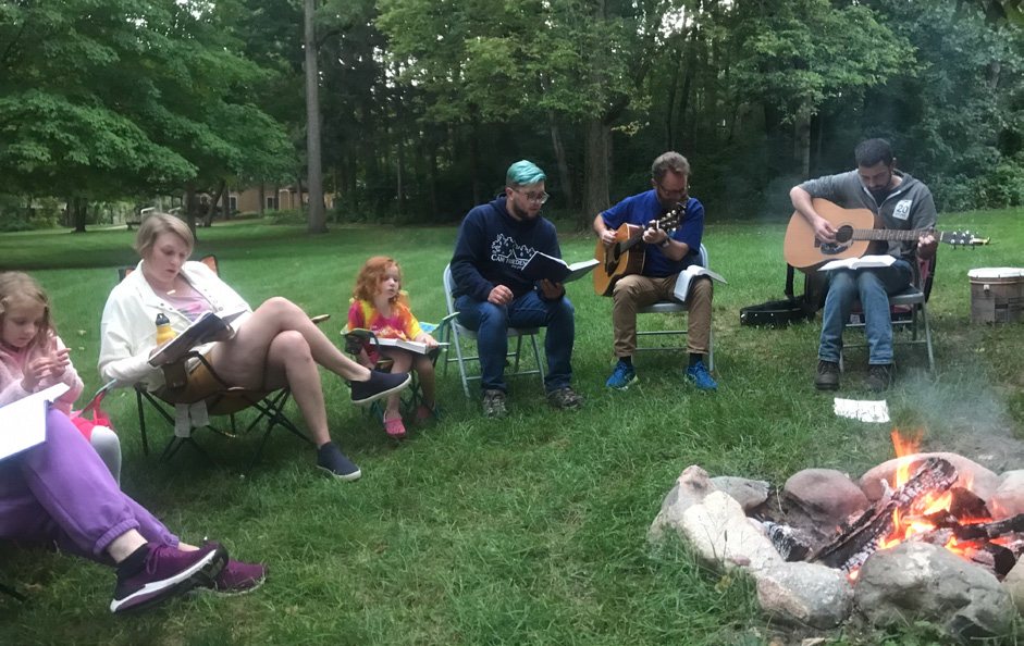 Members of Grand Rapids Mennonite Fellowship worship together outdoors around a campfire with guitars