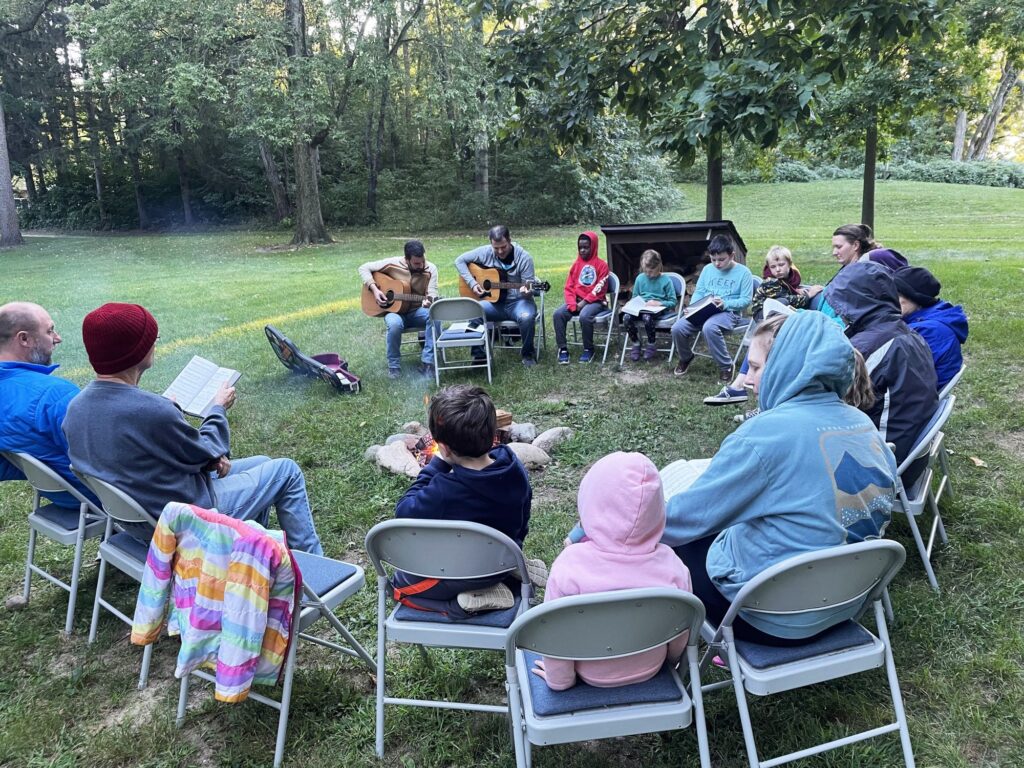 Grand Rapids Mennonite Fellowship worshiping outdoors in a circle of chairs with guitars
