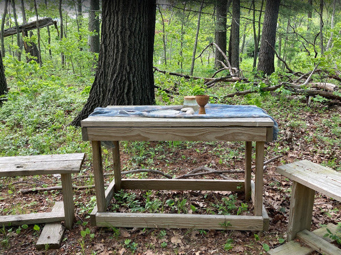 A wooden table in the woods set with a chalice and bread